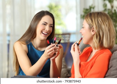 Two friends making up choosing lipstick sitting on a couch in the living room at home - Powered by Shutterstock