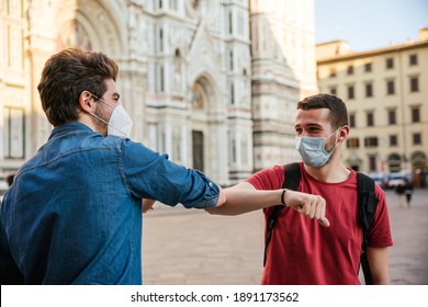 Two Friends Meet In The City Of Florence And Greet Each Other By Touching Their Elbows Without Shaking Hands For Fear Of Contagion Of Infections, They Wear Protective Face Masks To Protect Themselves 