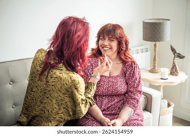 Two friends, a non-binary person and a curvy woman, sitting on a sofa, enjoying intimate moments of self-care while applying makeup and celebrating body positivity and friendship