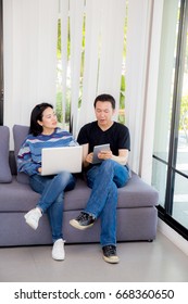 Two Friends On Line With Multiple Devices And Talking Sitting On A Sofa In The Living Room In A House Interior.