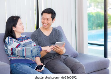 Two Friends On Line With Multiple Devices And Talking Sitting On A Sofa In The Living Room In A House Interior, Communication Concept.