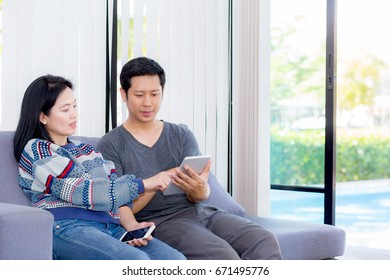 Two Friends On Line With Multiple Devices And Talking Sitting On A Sofa In The Living Room In A House Interior, Communication Concept.