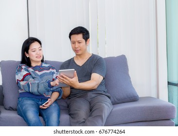 Two Friends On Line With Multiple Devices And Talking Sitting On A Sofa In The Living Room In A House Interior, Communication Concept.