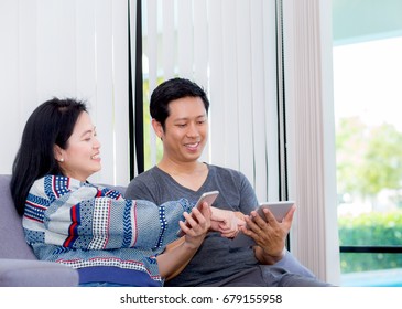 Two Friends On Line With Multiple Devices And Talking Sitting On A Sofa In The Living Room In A House Interior, Communication Concept.