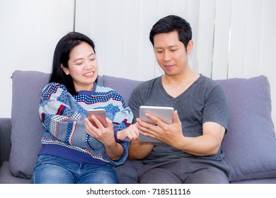 Two Friends On Line With Multiple Devices And Talking Sitting On A Sofa In The Living Room In A House Interior, Communication Concept.