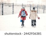 Two friends overcoming a winter snowstorm as they walk through the snow, in a snowfall