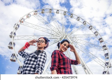 Two friends posing in camera with ferris wheel in background - Girls dressed in pin up 50's style - Fashion lifestyle concept - Warm filter tihe soft vignette editing 
