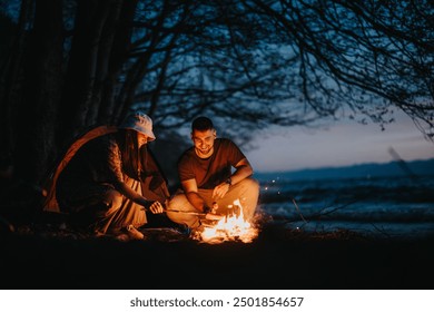 Two friends preparing dinner over a campfire by a lake, enjoying the peaceful outdoors at night. - Powered by Shutterstock