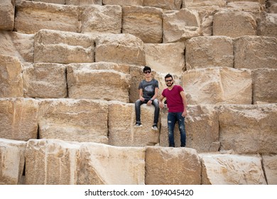 Two friends in the pyramids together one sitting one standing on the huge stone of the pyramid.