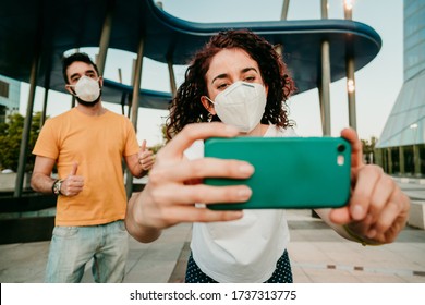 
Two Friends Reuniting After A Long Time After The Quarantine Caused By The Covid19. They Wear A Surgical Mask And Take Photos Together With Social Distance