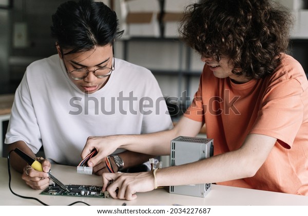Two Friends Secondary School Students at the tech\
lab soldering together electronics circuit board device in the\
science technology workshop - Digital Innovation in Education.\
Cooperation at school