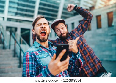 Two friends showing sincere emotions of joy about victory in online lottery. Men being happy winning a bet in online sport gambling application with football stadium on the background. 