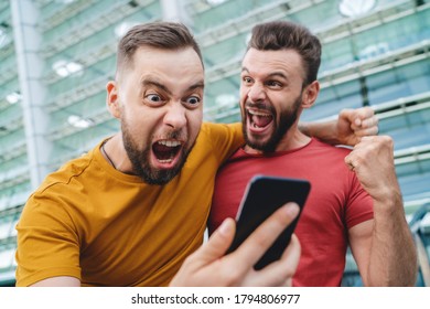 Two friends showing sincere emotions of joy about victory in online lottery. Men being happy winning a bet in online sport gambling application with football stadium on the background.  - Shutterstock ID 1794806977