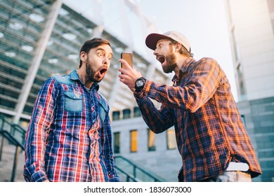 Two Friends Showing Sincere Emotions Of Joy About Victory In Online Lottery. Men Being Happy Winning A Bet In Online Sport Gambling Application With Football Stadium On The Background.