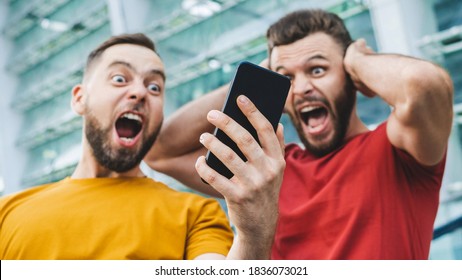 Two friends showing sincere emotions of joy about victory in online lottery. Men being happy winning a bet in online sport gambling application with football stadium on the background. - Shutterstock ID 1836073021