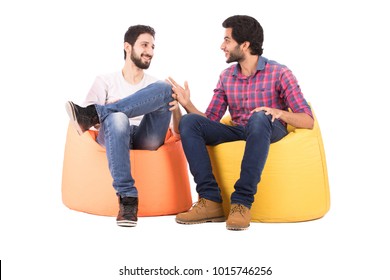 Two Friends Sitting On Beanbags Talking, Smiling, Looking Happy, Isolated On A White Background.