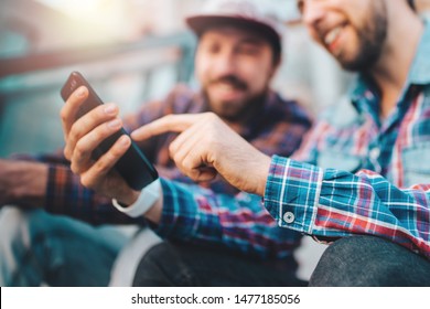 Two friends sitting on football stadium steps and making bets using gambling mobile application. Men watching online broadcast waiting for winner results ready to celebrate victory. Focus is on hand. - Powered by Shutterstock