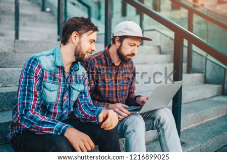 Two friends sitting on football stadium steps, after betting in online sport bookmaker, and watching broadcast on laptop waiting for winner results ready to celebrate victory.
