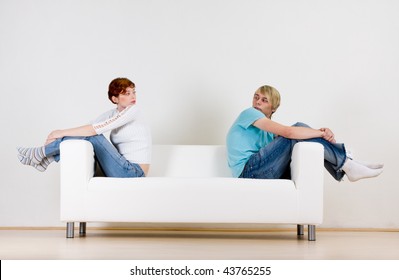 Two Friends Sitting On Opposite Ends Of A White Couch.