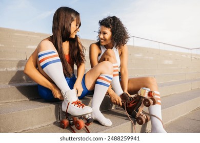 Two friends sitting on steps, putting on their roller skates and smiling at each other, ready for a fun skating session. - Powered by Shutterstock