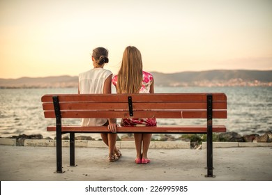 two friends sitting on wood bench near beach on evening sunset - Powered by Shutterstock