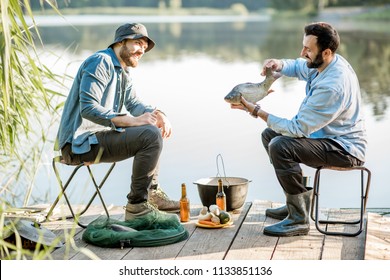 Two friends sitting together with beer and fish on the picnic while fishing near the lake - Powered by Shutterstock