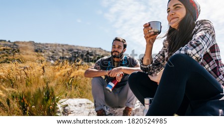 Two friends taking a break while hiking. Woman drinking coffee and resting with friend on hike trip.