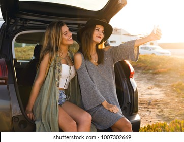 Two friends taking a selfie while sitting in the trunk of a car  - Powered by Shutterstock