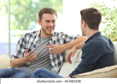 Two friends talking sitting in a couch in the living room with a window in the background at home