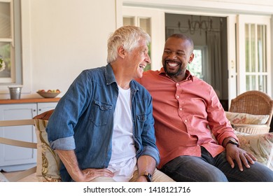 Two Friends Talking While Sitting On Couch In The Courtyard. Senior Man And African Guy Laughing While In Conversation Sitting Outside Home. Two Men Talking To Each Other And Enjoying.