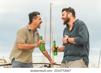 Two friends in their forties laughing heartily on the deck of a docked boat, wearing summer outfits and enjoying a joyful moment together holding beer bottles. - Powered by Shutterstock