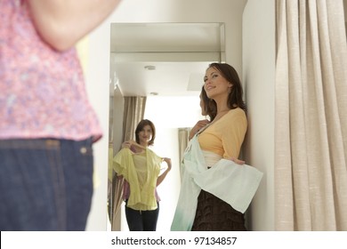 Two friends trying clothes on in a fashion store's fitting room.