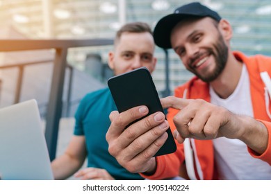 Two friends using mobile phone and laptop for betting during soccer play ready to celebrate victory of favourite team. Men using gambling application while sitting on stadium steps. Focus is on hand. - Powered by Shutterstock