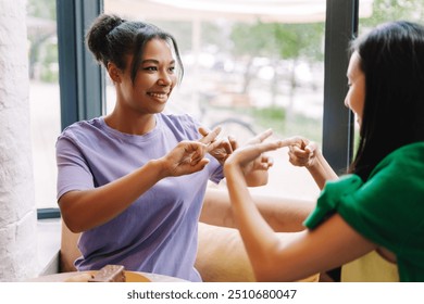Two friends are using sign language while having a pleasant conversation in a cafe, enjoying each other's company over coffee and cake. Inclusion concept