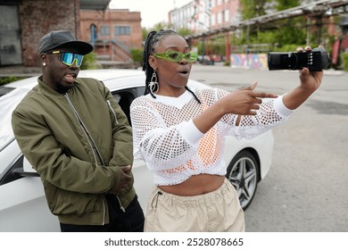 Two friends using a smartphone for taking selfie outdoors with graffiti walls and buildings in background, capturing a spontaneous moment of fun and excitement