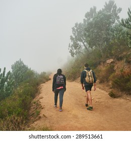 Two Friends Walking Away From The Camera On A Dirt Path In A Nature Reserve On A Misty Morning