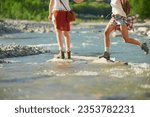 Two friends walking over rocks crossing a river during a hiking trip. Women on holiday on a hiking trip together crossing a river