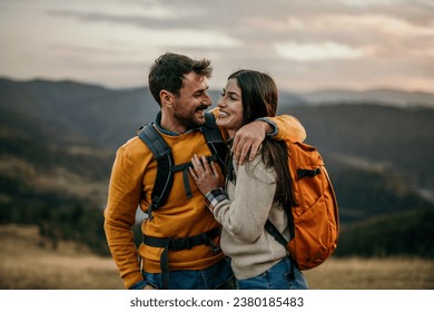 Two friends walking uphill with backpacks, catching sight of a serene lake - Powered by Shutterstock