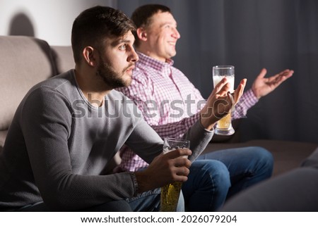 Two friends watching matchup on tv together, but supporting different teams
