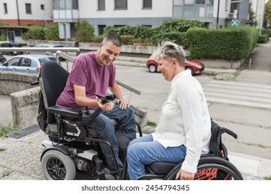 Two friends, wheelchair users on the street, smiling and looking at a smartphone. People with disability and social wellbeing concepts. - Powered by Shutterstock