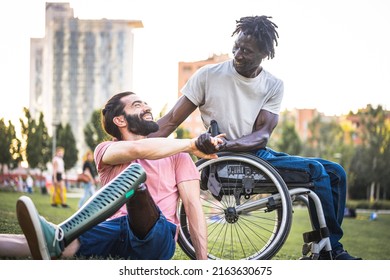 Two friends who greet each other at the park, adult African man in wheelchair shaking hands with his Hispanic friend with an artificial leg