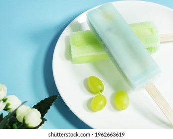 Two fruit popsicles and grapes in a white plate, relieving summer-heat, best food in summer, blue background - Powered by Shutterstock