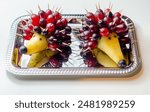 Two fruit shaped like hedgehogs are on a silver tray. The hedgehogs are made of grapes and pears