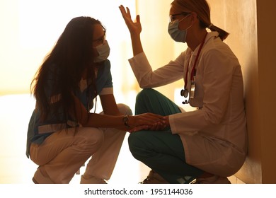 Two Frustrated Doctors In Protective Masks Sit In Hallway