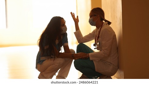 Two frustrated doctors in protective masks sit in hallway. Burnout syndrome in work of doctors concept - Powered by Shutterstock