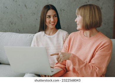 Two fun adult IT women mature mom young kid wear casual clothes work hold use laptop pc computer sit on gray sofa couch stay home flat rest relax spend free spare time in living room. Family concept - Powered by Shutterstock