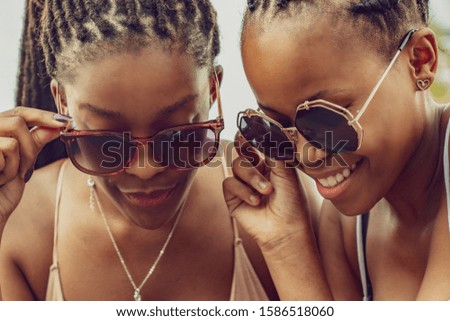 Two fun African girls wearing sunglasses taking selfie outdoors.