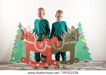 Two funny boys in a Santa Claus hat are playing with horses drawn on cardboard. The guys have fun at home. Christmas holiday concept. Copy space.