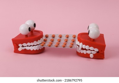 Two Funny  Clockwork Jumping Teeth Toy With Pills On Pink Background.