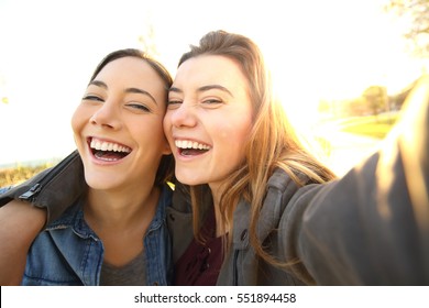 Two funny friends taking selfie outdoors in the street at sunset with a warm light in the background